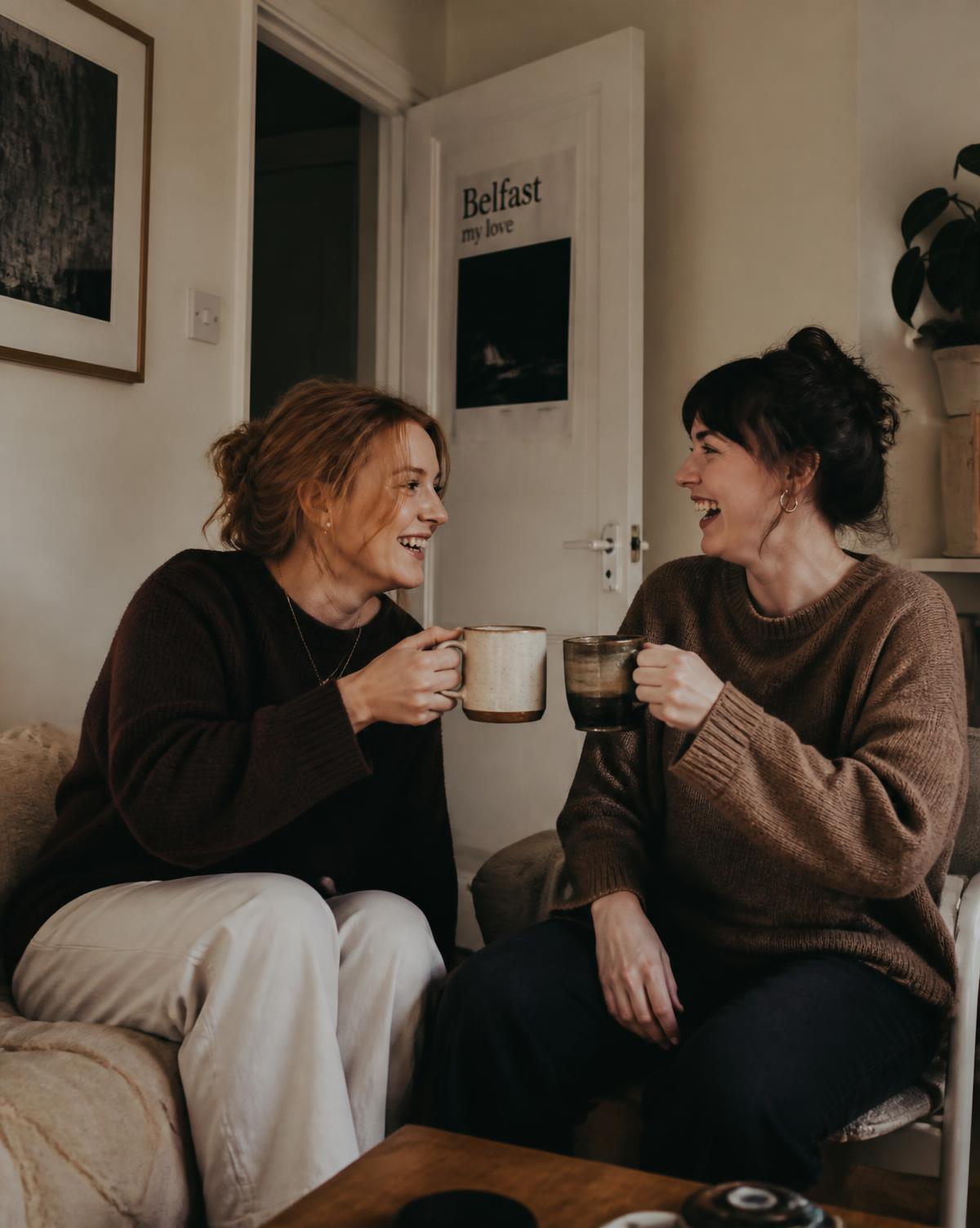 Two friends in a Belfast flat raising mugs together in celebration